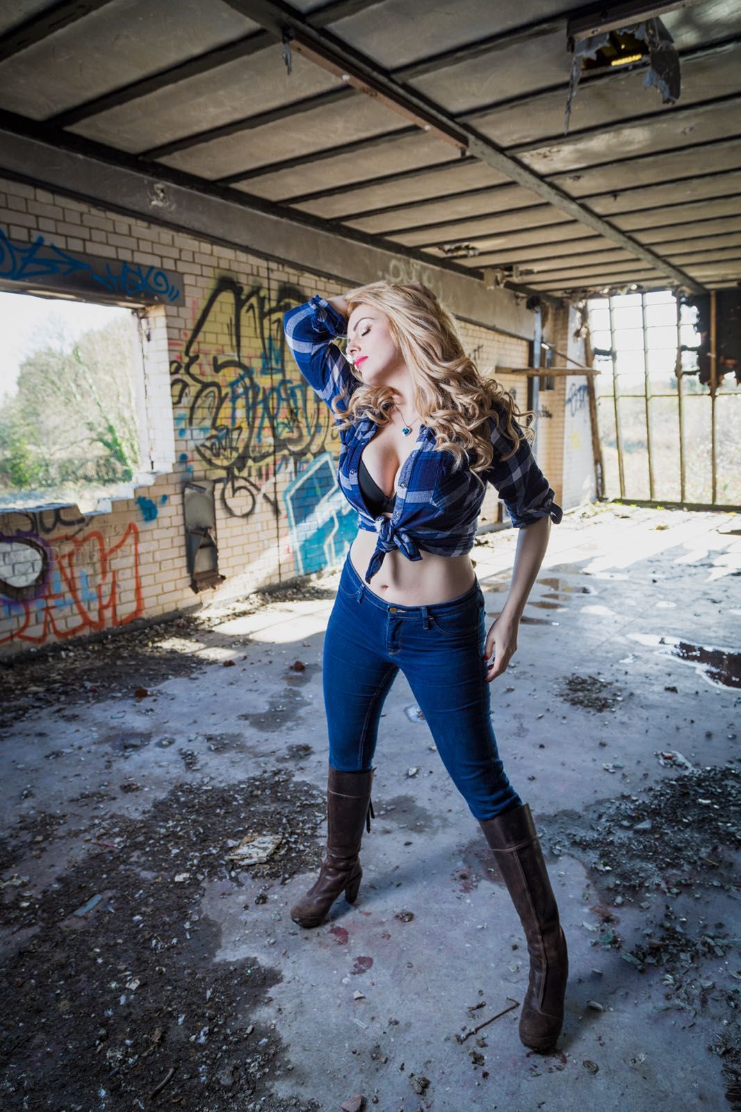 fashion model in derelict building wearing blue jeans ans shirt with long leather boots 