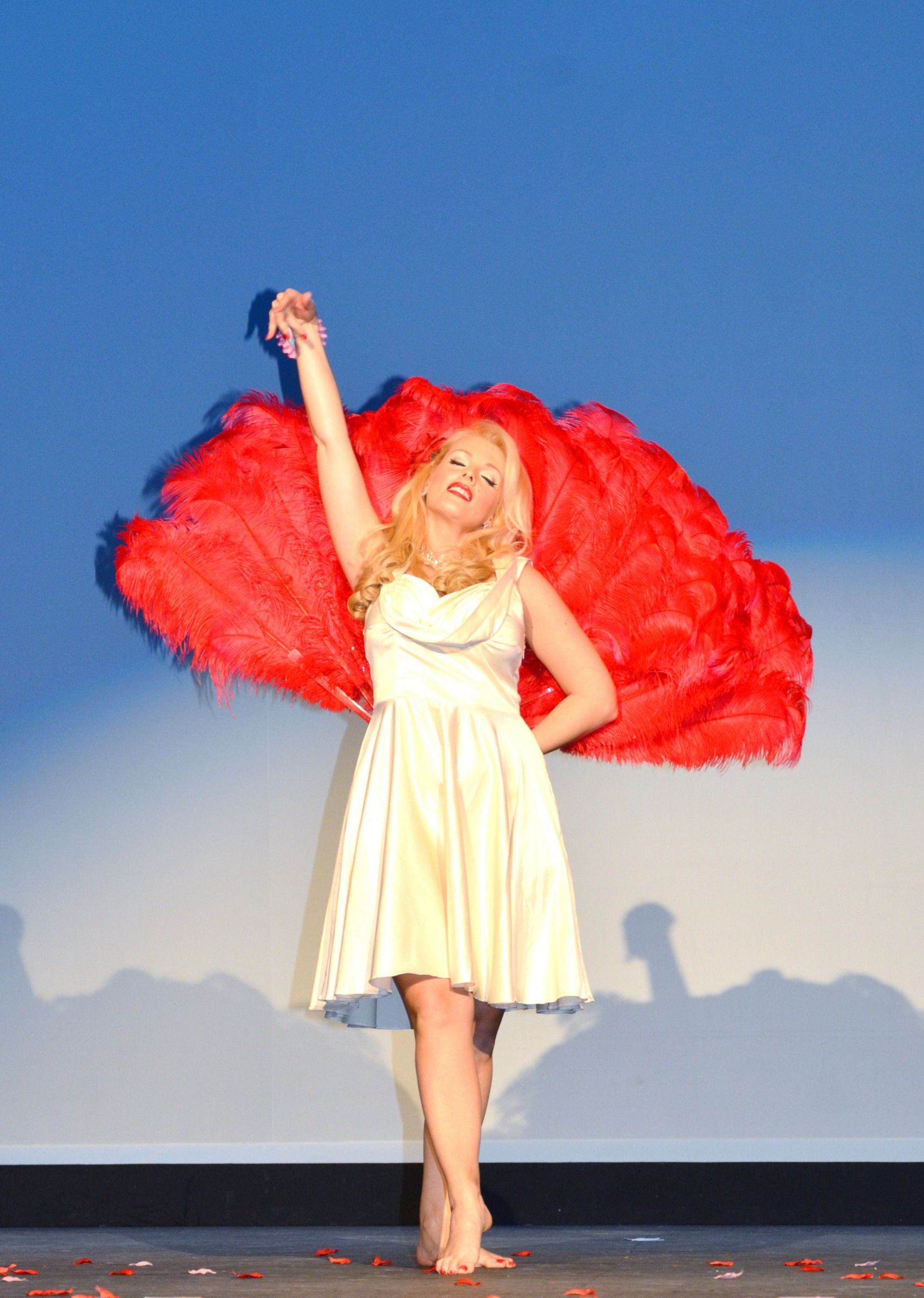 performing feathered kisses act holding large red feathered hand fans behind back