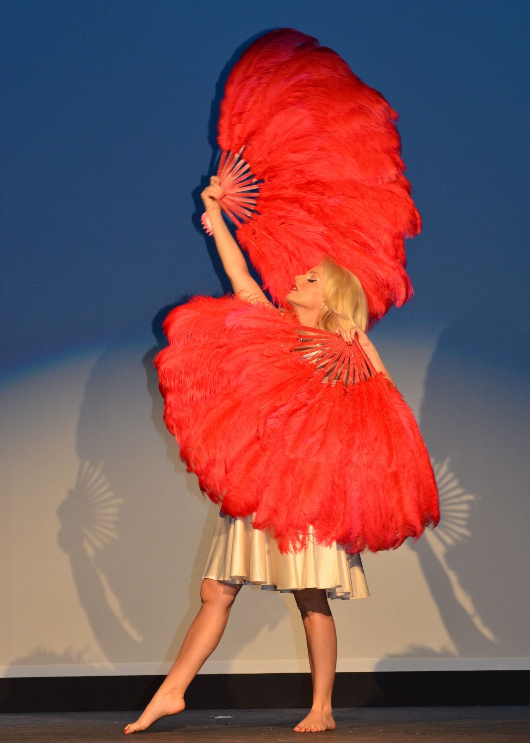 feathered kisses act standing side on holding large red feathered hand fans in front and behind